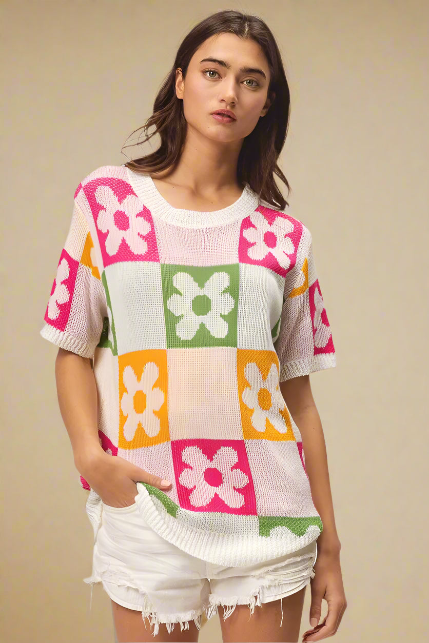 Woman wearing a colorful checkered sweater with floral patterns on a plain background