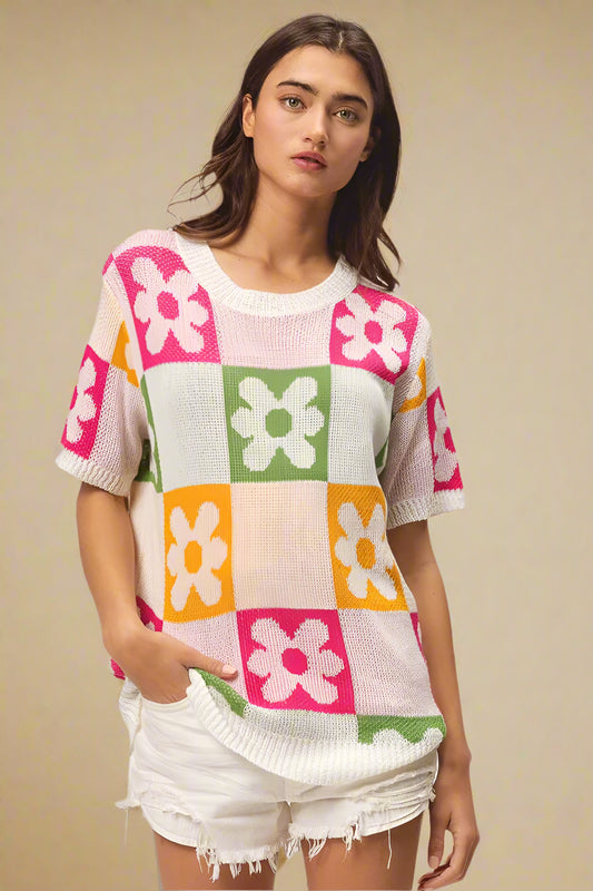 Woman wearing a colorful checkered sweater with floral patterns on a plain background