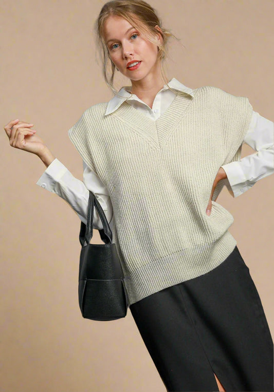 Woman wearing a cream-colored poncho over a white shirt with a black handbag on a beige background