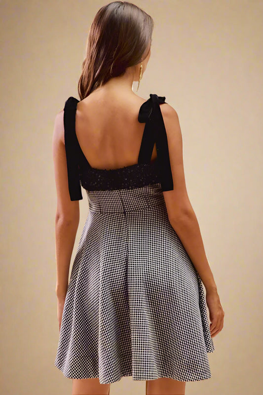 Woman wearing a black top and gray checkered skirt against a beige background