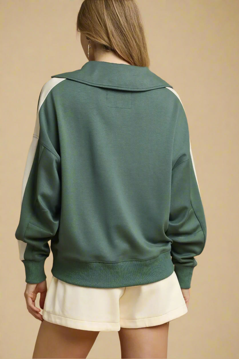 Green sweatshirt with white accents worn by a person on a beige background