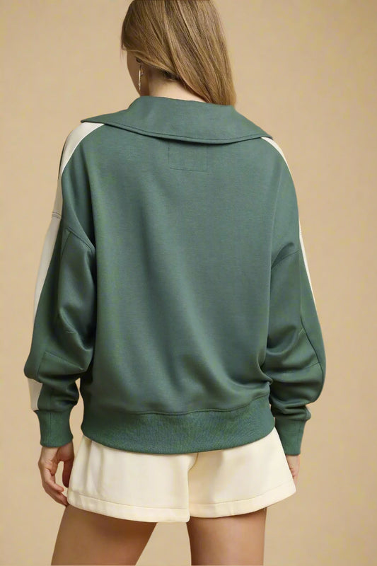 Green sweatshirt with white accents worn by a person on a beige background