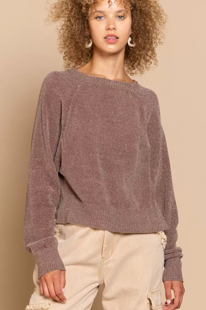 Woman wearing a brown sweater and beige pants against a beige background