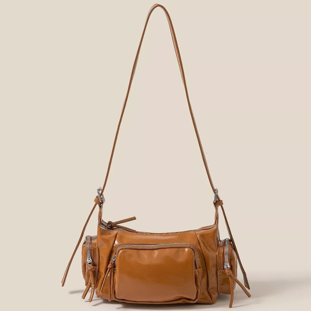 Brown leather handbag with multiple pockets and a long strap on a beige background