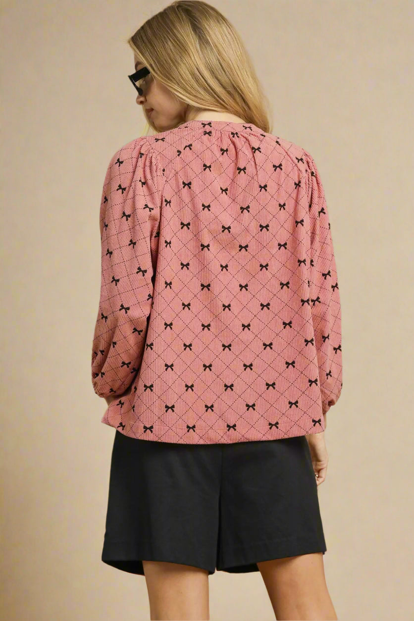 Woman wearing a pink blouse with black patterns and black shorts on a beige background