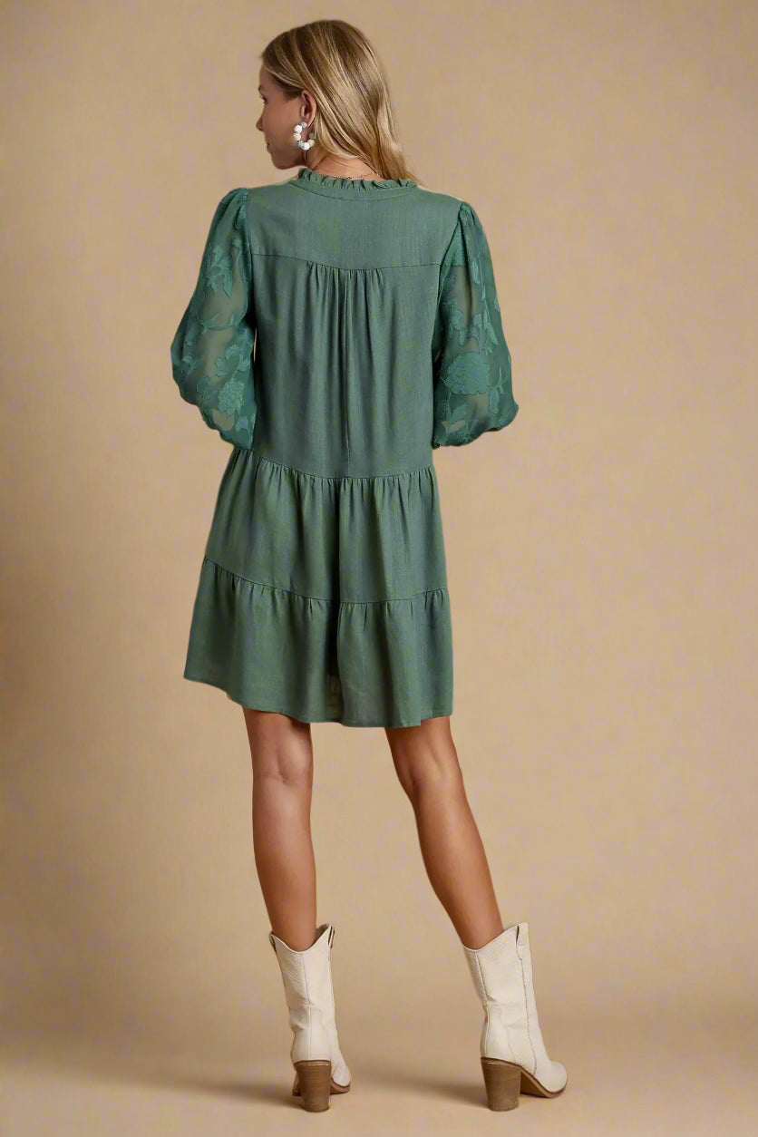 Woman wearing a green dress with long sleeves and a tiered skirt on a beige background.