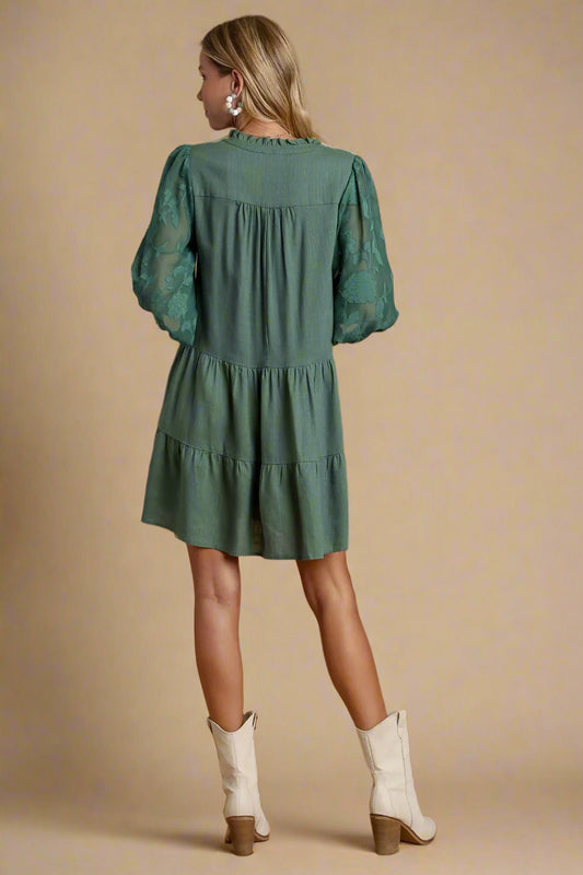 Woman wearing a green dress with long sleeves and a tiered skirt on a beige background.