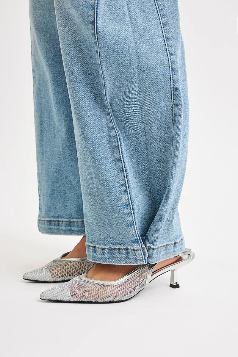 Close-up of silver high-heeled shoes worn with light blue jeans on a white background