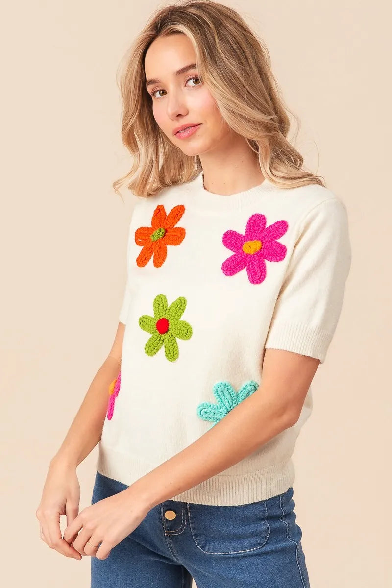 Woman wearing a cream sweater with colorful flower patterns on a beige background