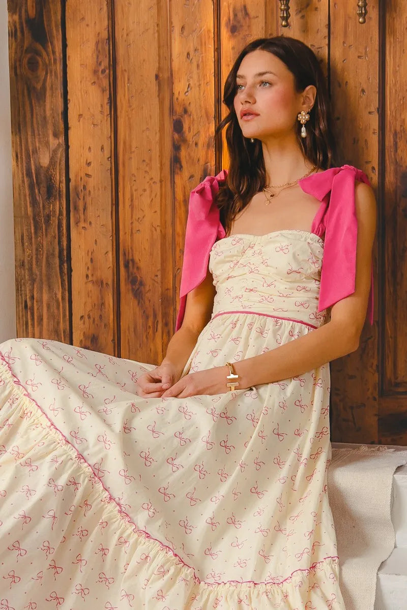 Woman in a floral dress with pink accents sitting against a wooden wall.
