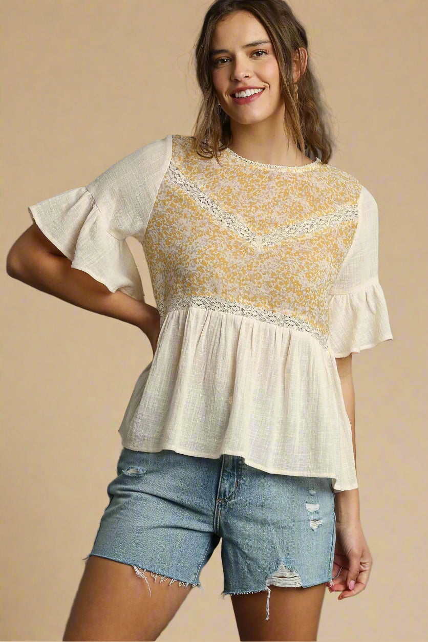 Woman wearing a cream and yellow floral blouse with denim shorts on a beige background