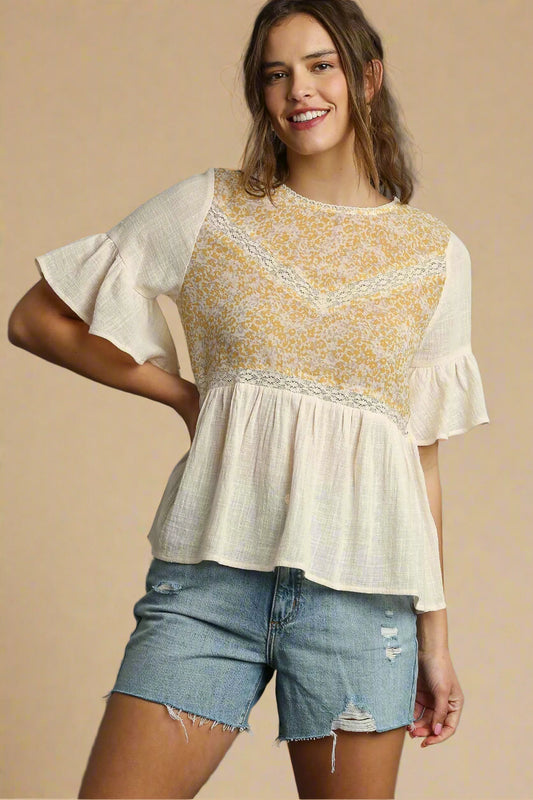 Woman wearing a cream and yellow floral blouse with denim shorts on a beige background