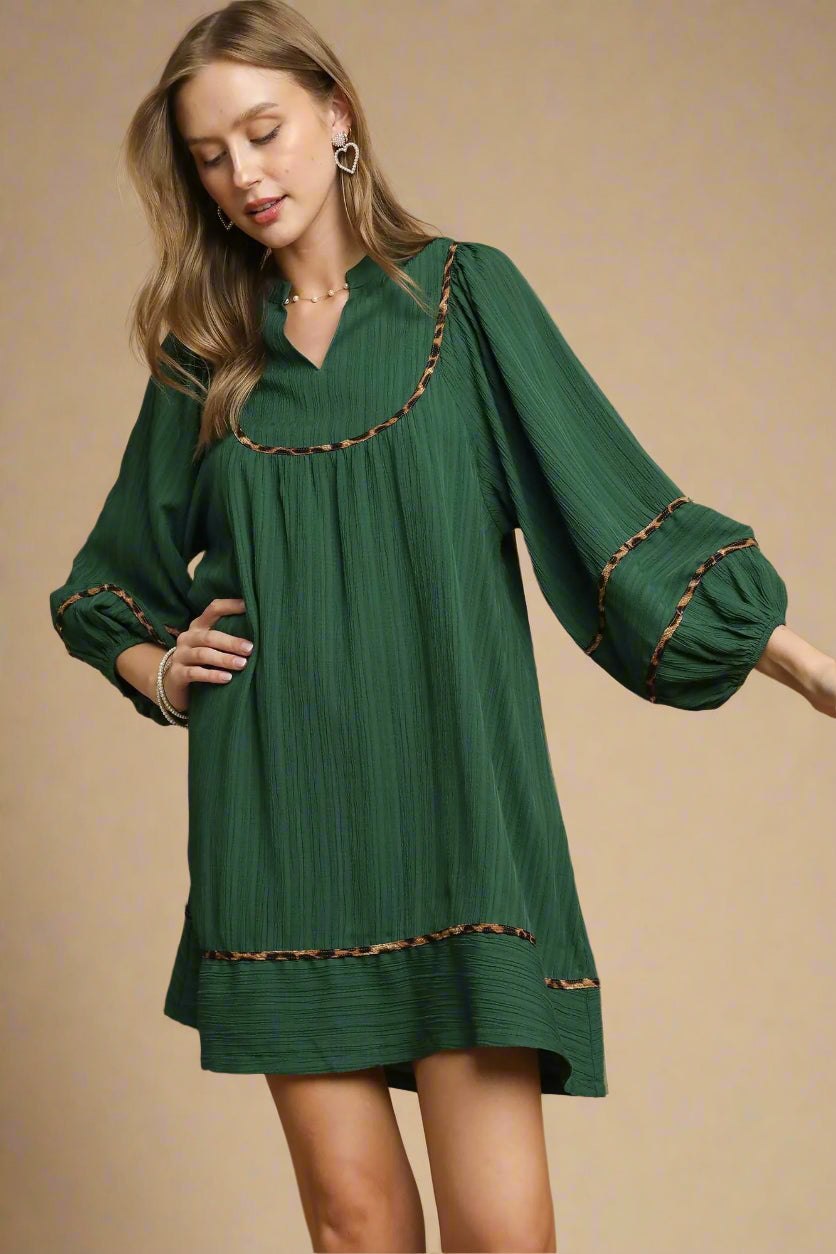 Woman wearing a green dress with brown trim on a beige background