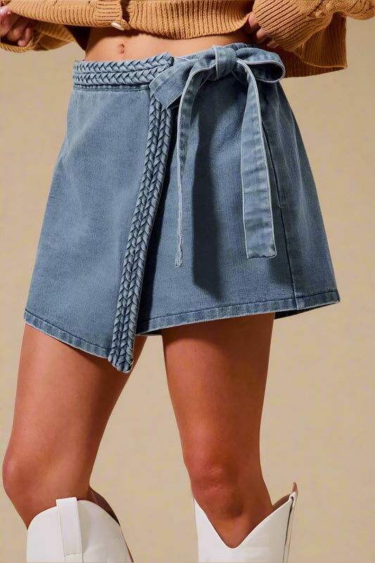 Person wearing a denim skirt with braided detail and white boots on a beige background