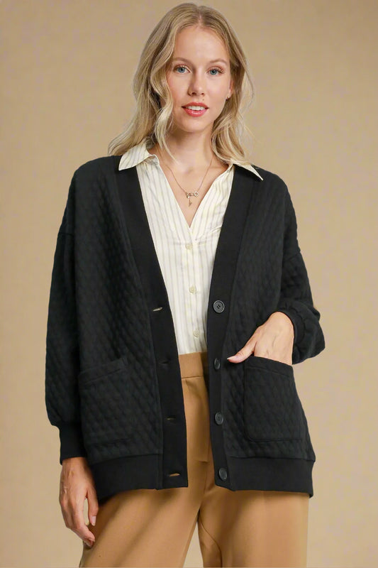 Woman wearing a black cardigan over a white shirt and tan pants on a beige background