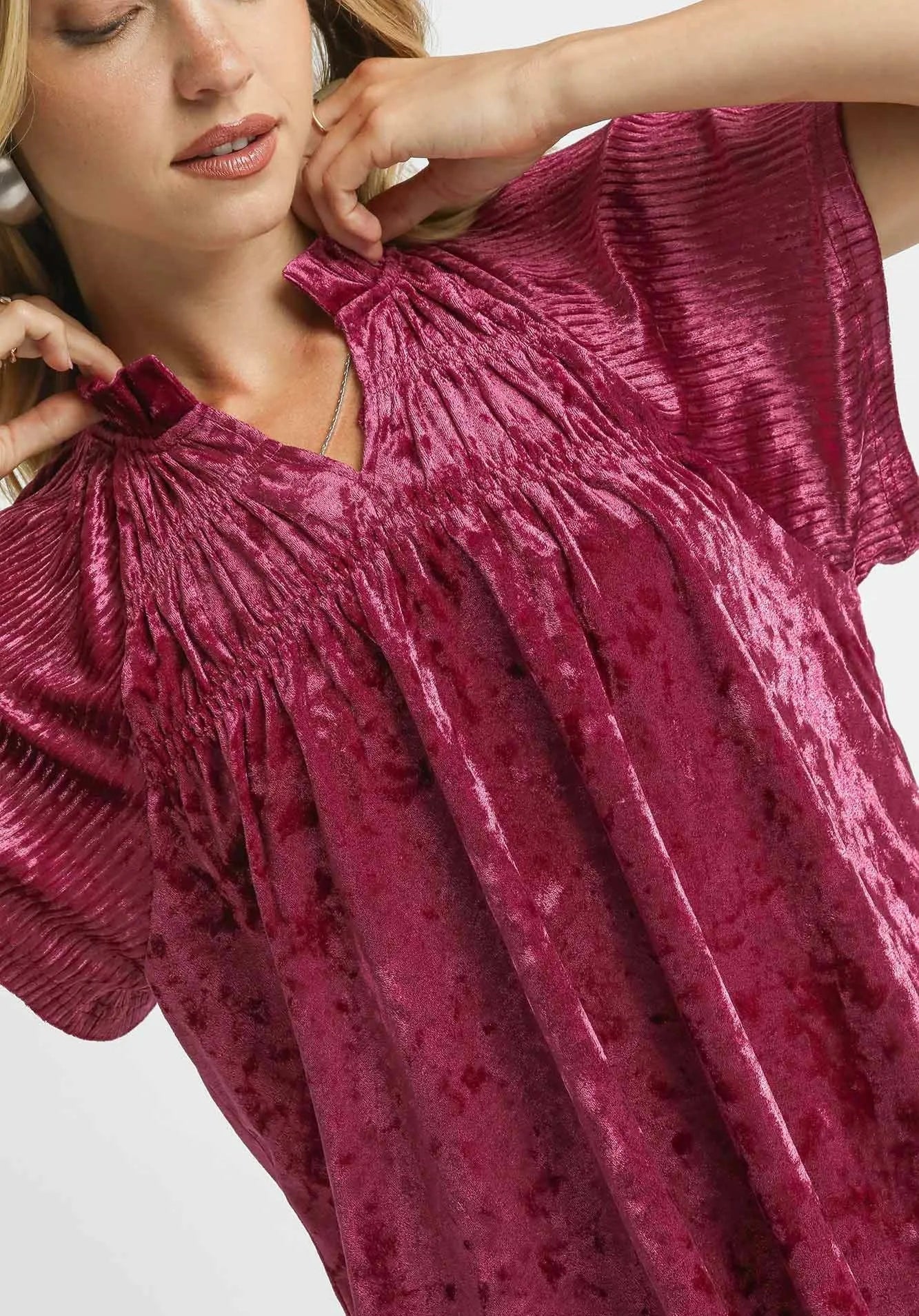 Close-up of a person wearing a burgundy velvet top with a plain background