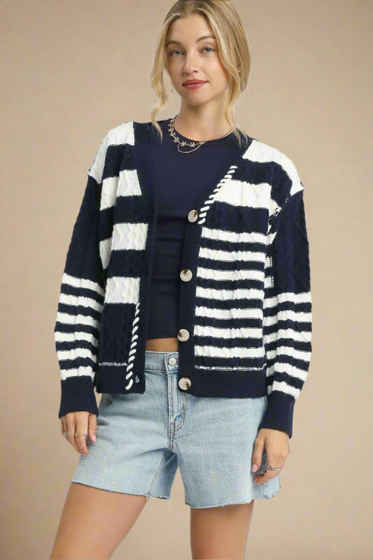 Woman wearing a navy and white striped cardigan over a black top and denim shorts on a light beige background.