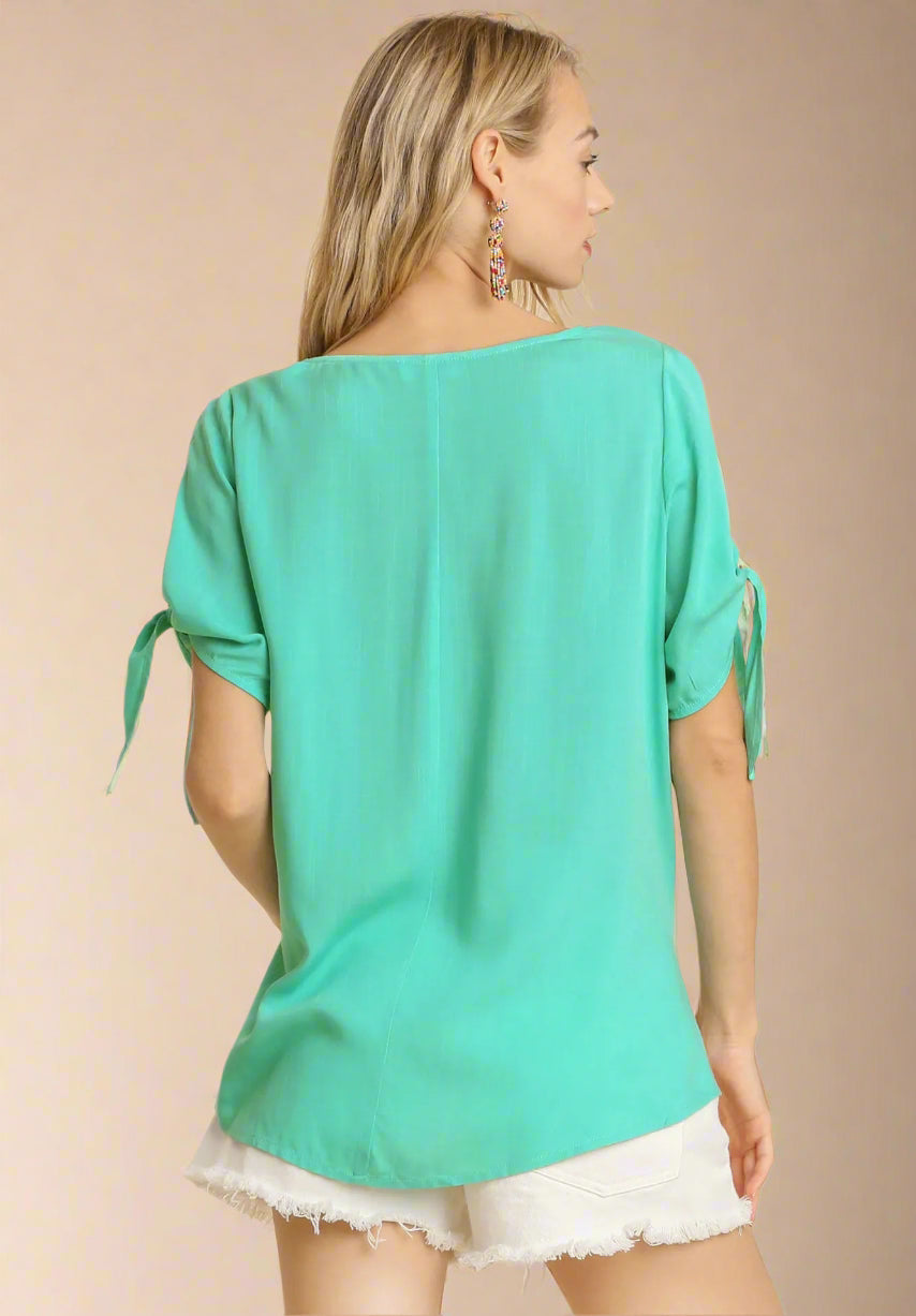 Woman wearing a teal top with tie sleeves on a beige background