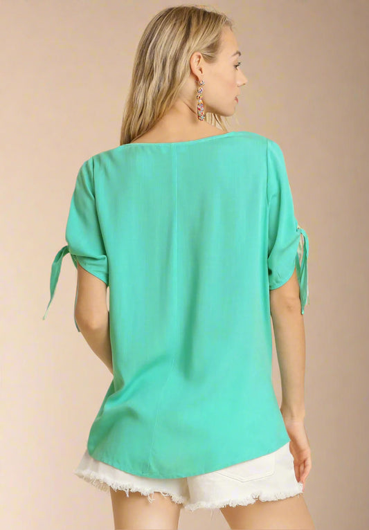 Woman wearing a teal top with tie sleeves on a beige background