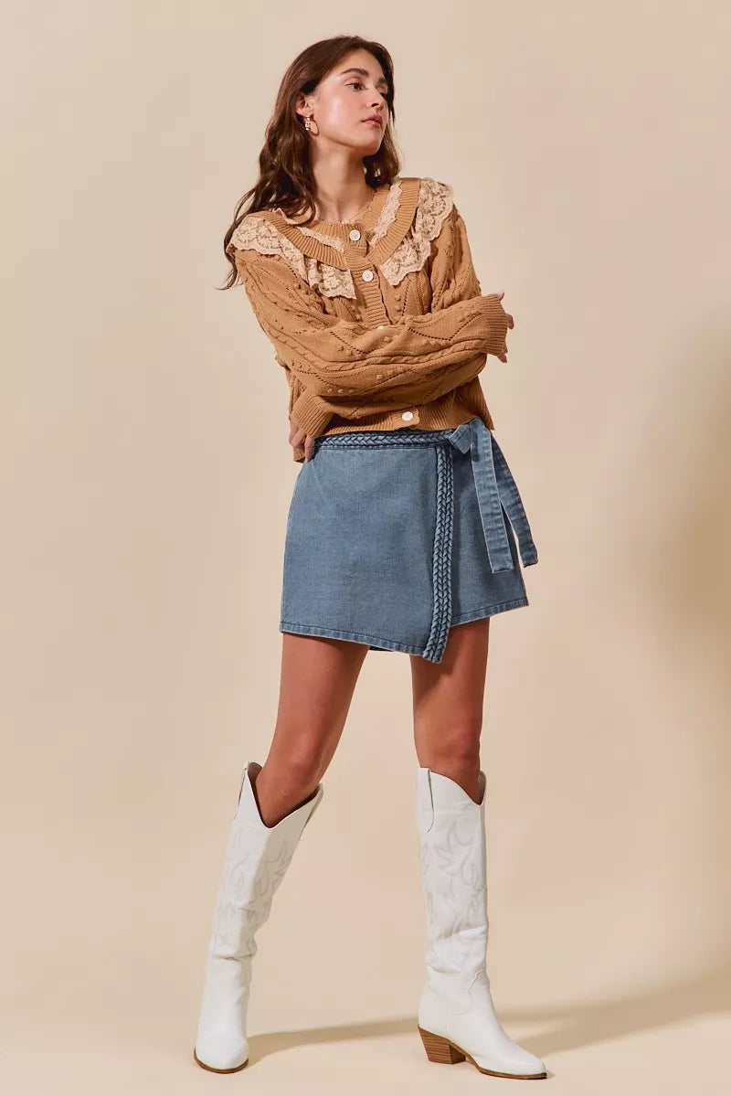 Woman wearing a brown sweater, denim skirt, and white knee-high boots on a beige background