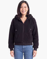 Beach Rose Co. black teddy fleece zip-up hooded jacket with a relaxed fit and ribbed cuffs worn with blue jeans.