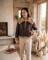 Beach Rose Co. brown faux leather aviator jacket with tan faux shearling collar and cuffs in a cozy living room.