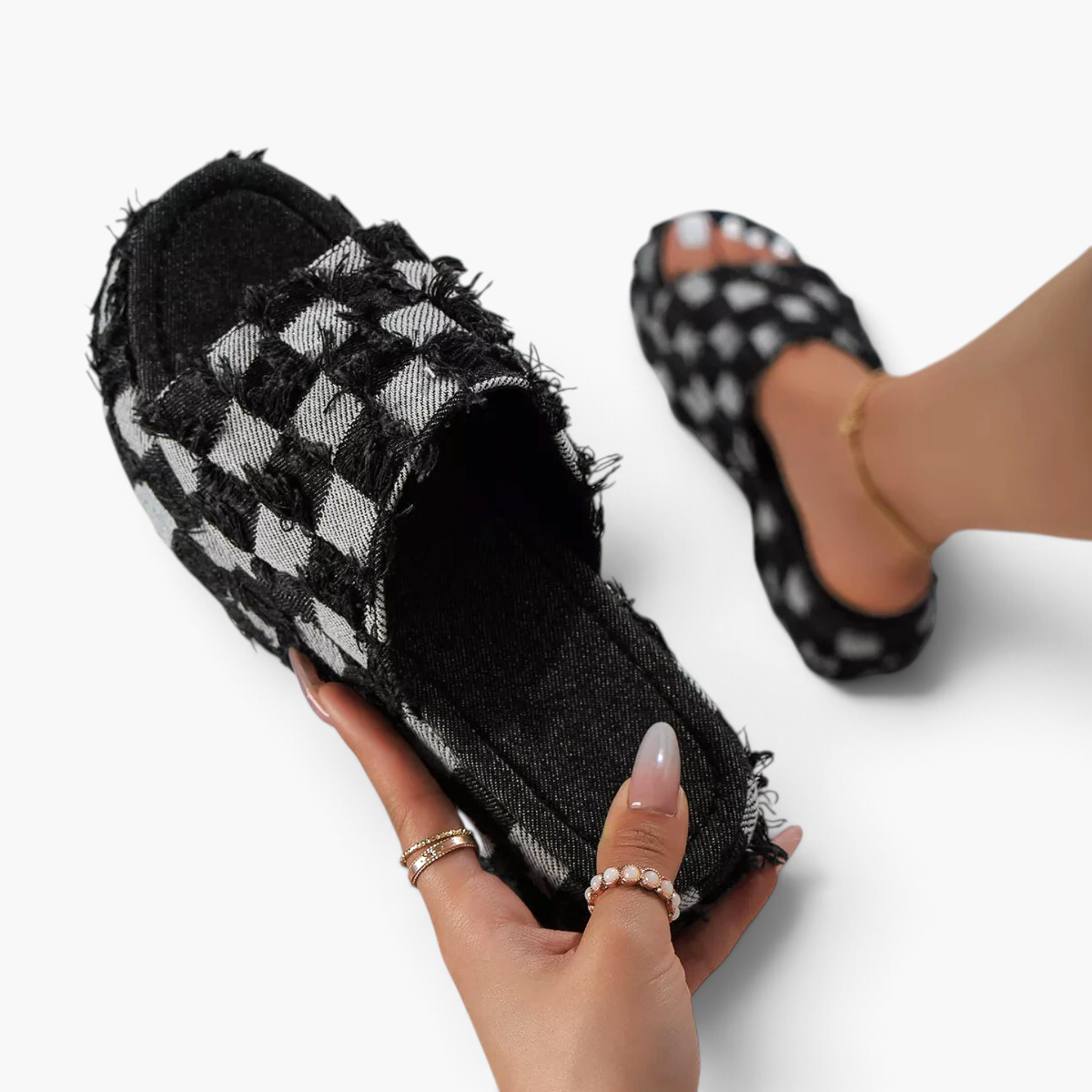 Beach Rose Co. black and white checkered denim platform slides with frayed edges held in hand.