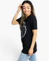 A woman modeling a black short-sleeve t-shirt with a large white graphic print on the front, paired with light blue jeans, against a plain white background.