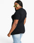 A woman wearing a black short-sleeve t-shirt and light blue jeans, shown from a side-back angle against a plain white studio background.