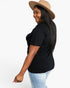 A woman wearing a black short-sleeve t-shirt, light wash blue jeans, and a beige wide-brim hat, shown from a side-back angle against a plain white studio background.
