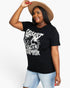 A woman wearing a black graphic t-shirt with a white distressed western-style print that reads 'DESERT RANGER', paired with light blue jeans and a tan wide-brim hat, against a plain white background.