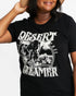 A woman wearing a black graphic t-shirt with a white western-style bull skull and 'DESERT DREAMER' text print, set against a plain light gray background.