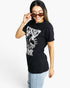 A woman modeling a black short-sleeve graphic t-shirt with a white distressed print on the front, paired with light blue jeans and dark sunglasses, against a plain white background.