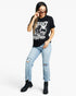 A woman modeling a black graphic t-shirt with a white skull print, paired with light-wash distressed jeans and black ankle boots, against a plain white background.