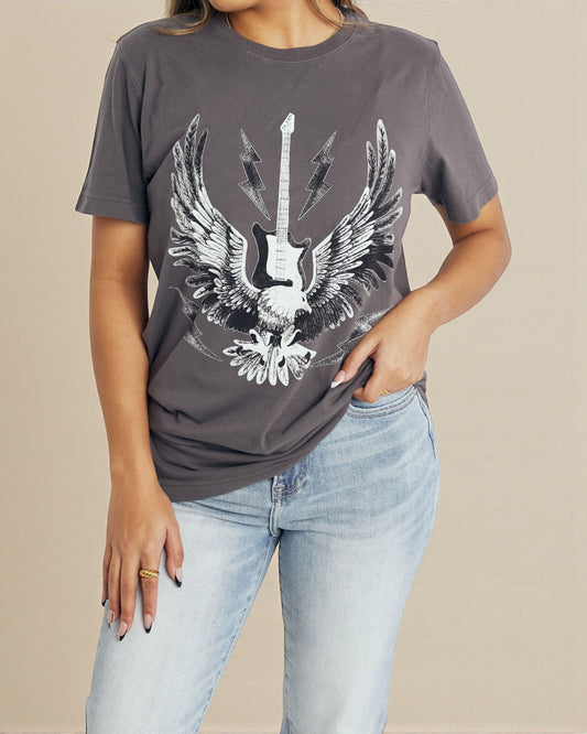 Person wearing a gray t-shirt with a guitar and wings design, standing against a beige background.
