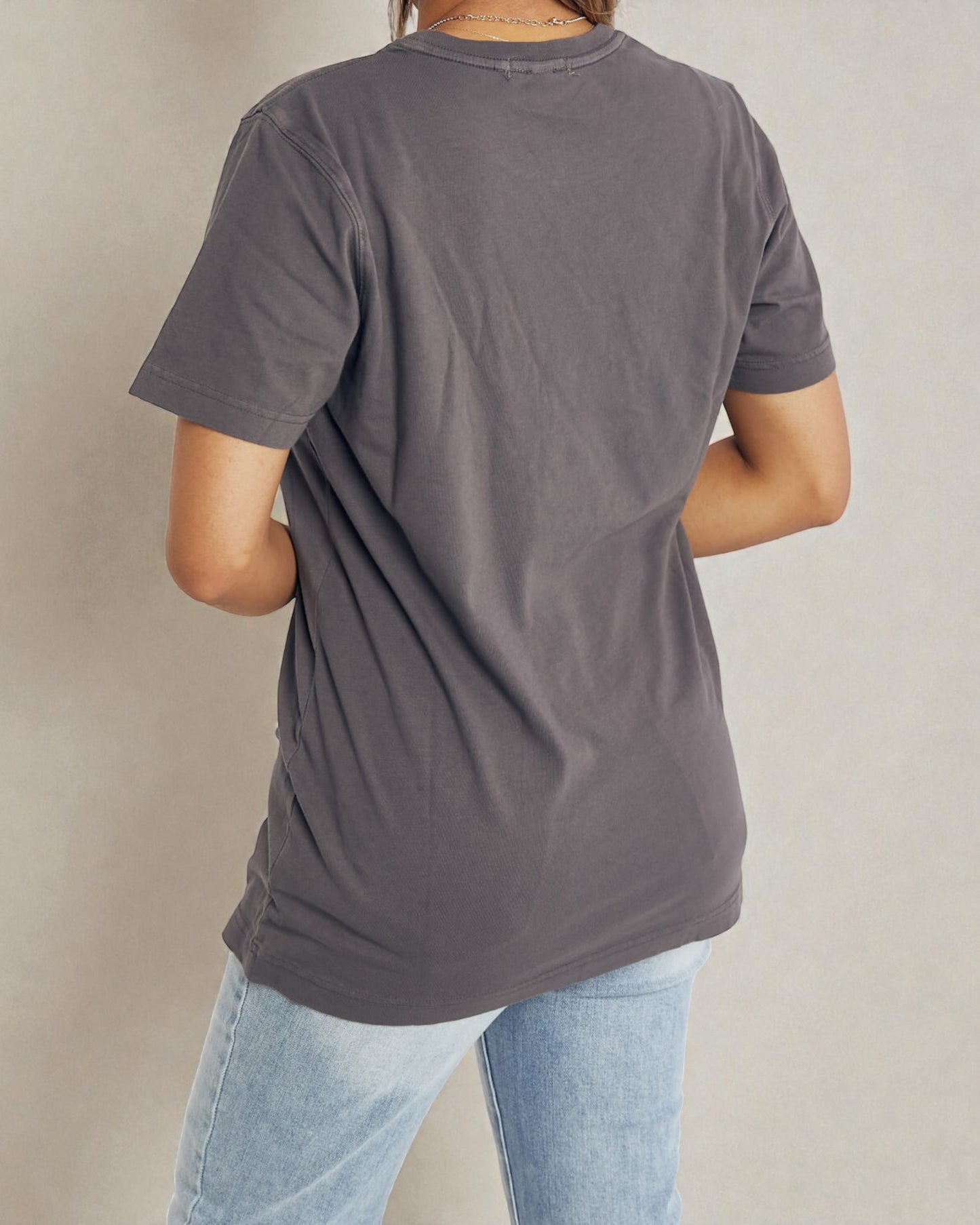Person wearing a gray t-shirt and light blue jeans against a beige background
