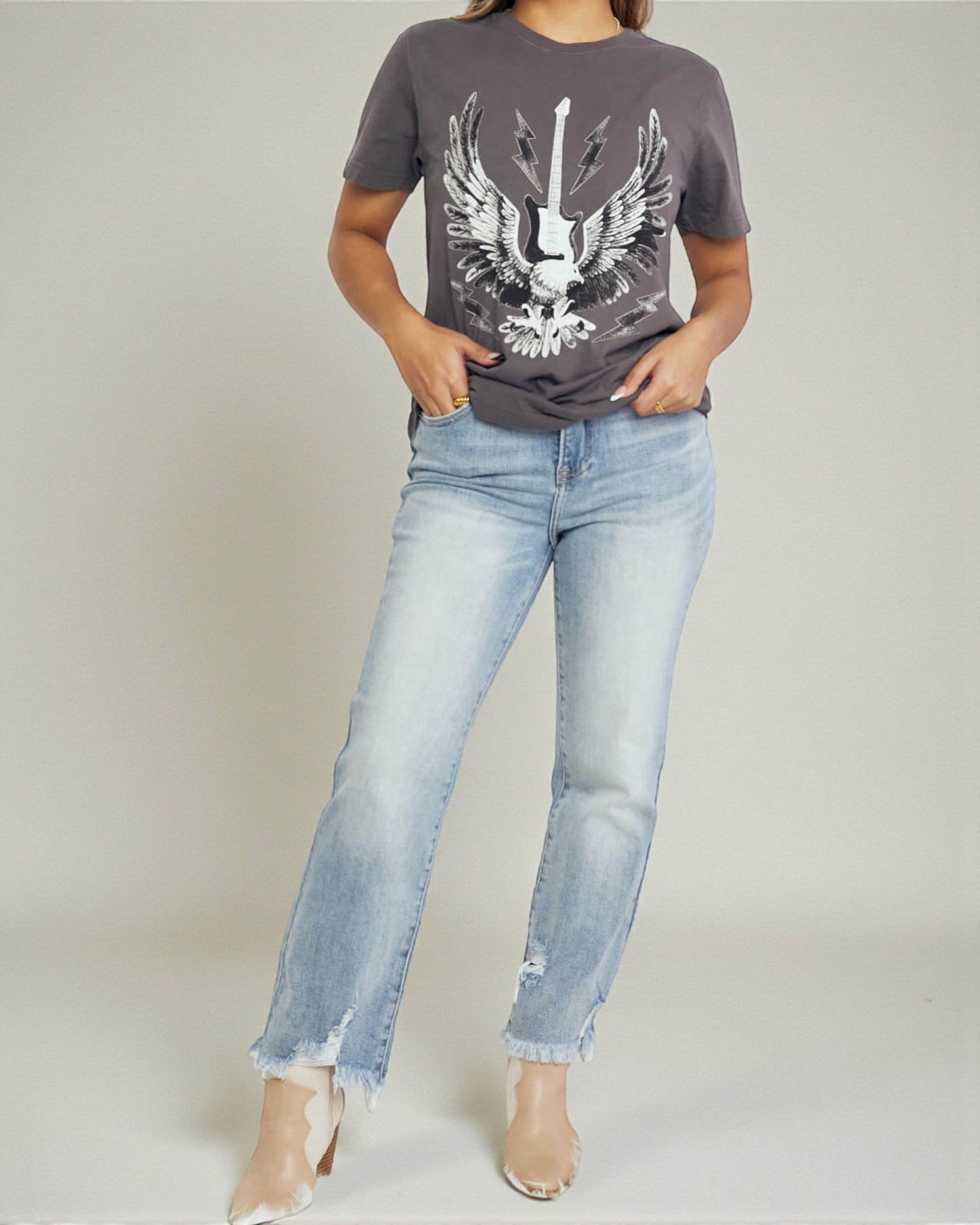 Person wearing a gray t-shirt with an eagle design and light blue jeans on a plain background