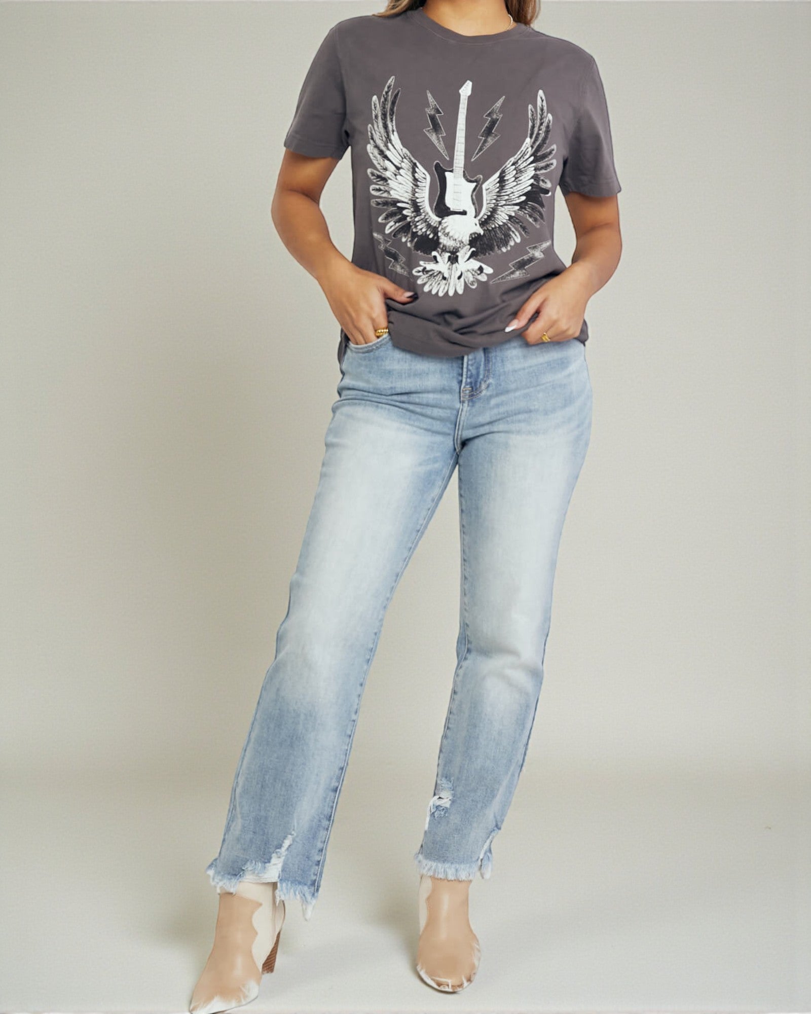 Person wearing a gray t-shirt with an eagle design and light blue jeans on a plain background