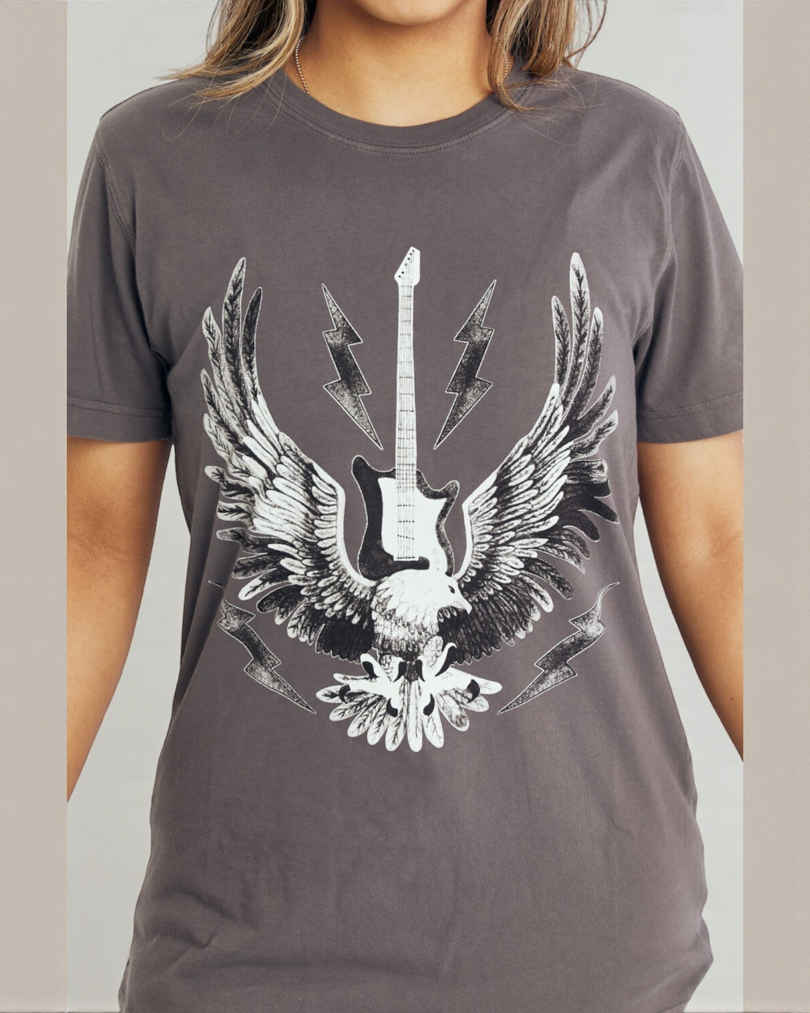 Person wearing a gray t-shirt with a graphic design of an eagle holding a guitar.