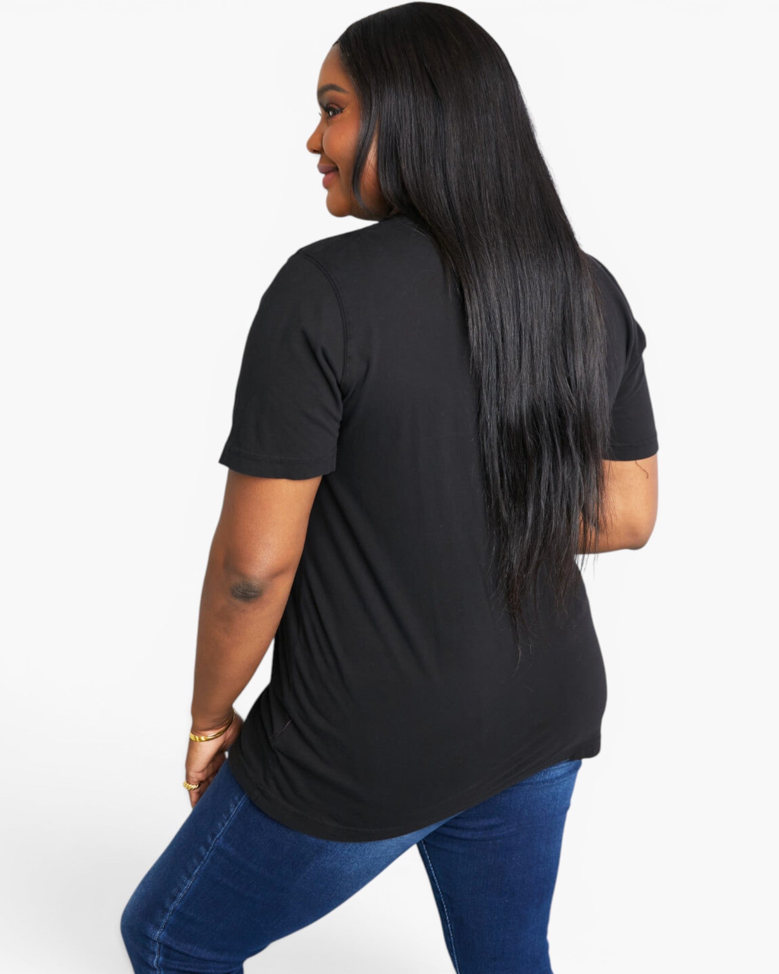 A woman with long, straight black hair is shown from the back wearing a black short-sleeve t-shirt and blue jeans against a plain white studio background.