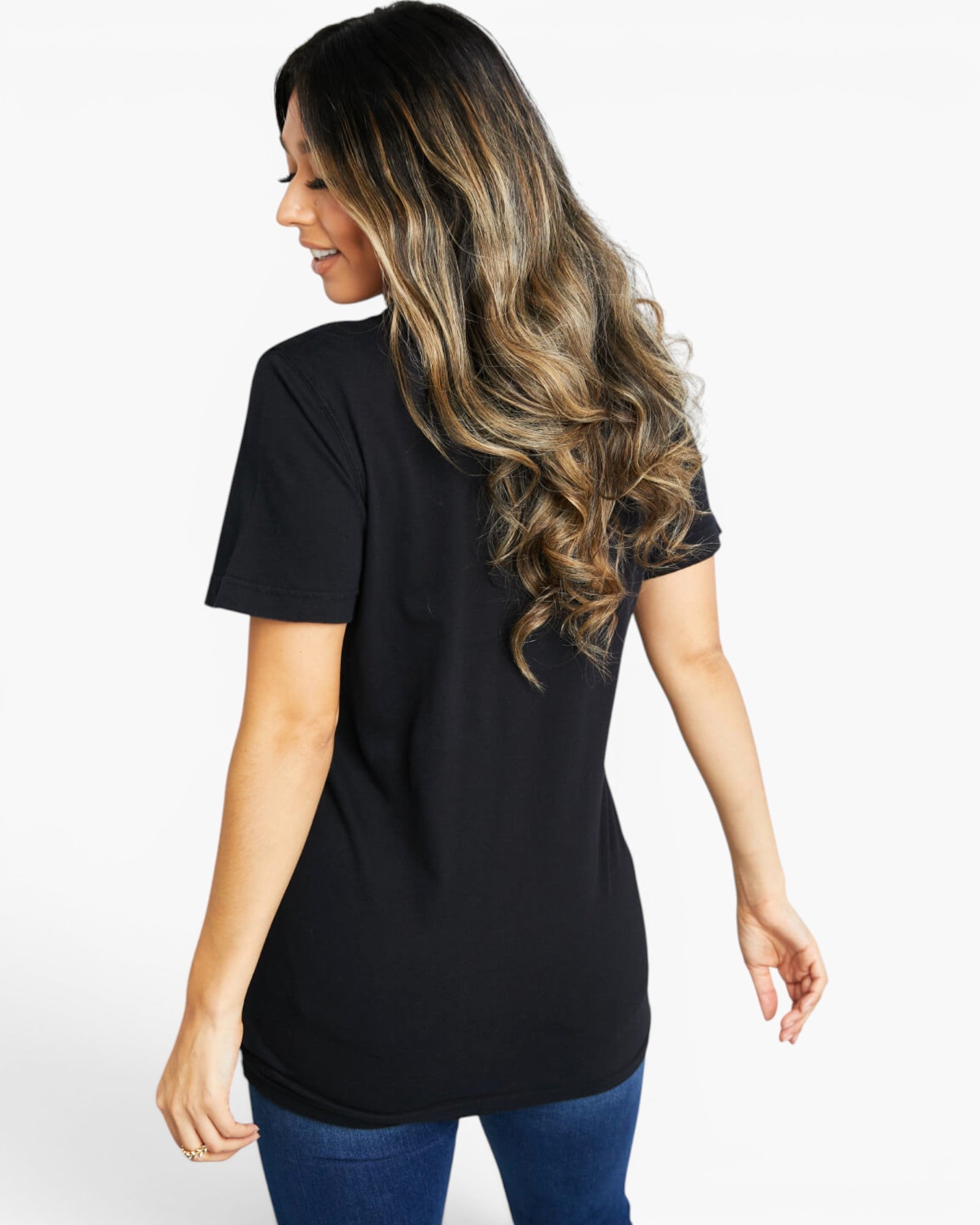 A woman with long highlighted hair is shown from the back wearing a black short-sleeve t-shirt and blue jeans against a plain white studio background.