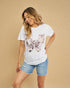 Woman wearing a white t-shirt with floral design and denim shorts on a beige background