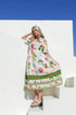 Woman wearing a colorful dress with floral patterns and text, standing against a white wall with blue sky.