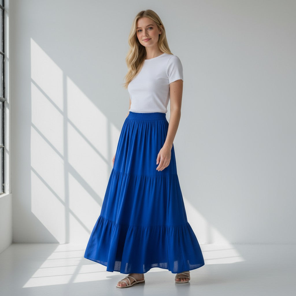Woman wearing a white top and blue skirt standing in a bright room with sunlight filtering through.