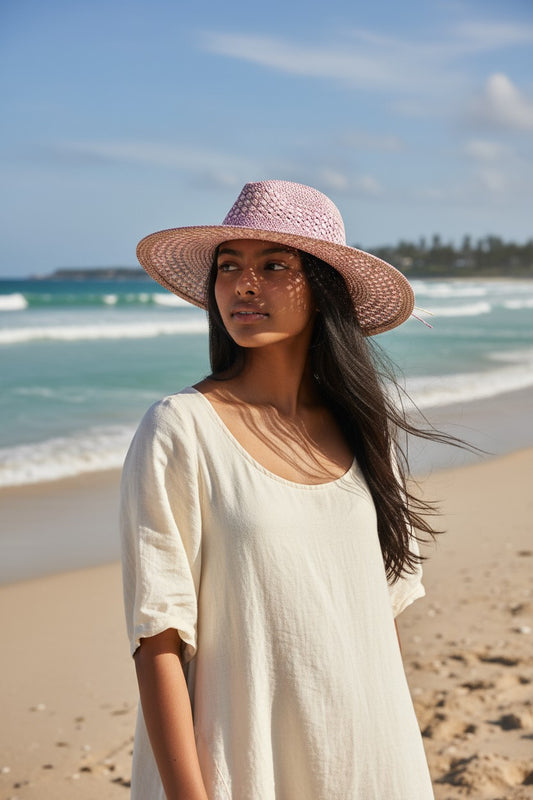 Woman wearing a wide-brimmed hat on a beach with ocean and sky in the background